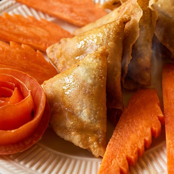 Golden fried samosas with carved carrot and tomato garnishes on a white plate.