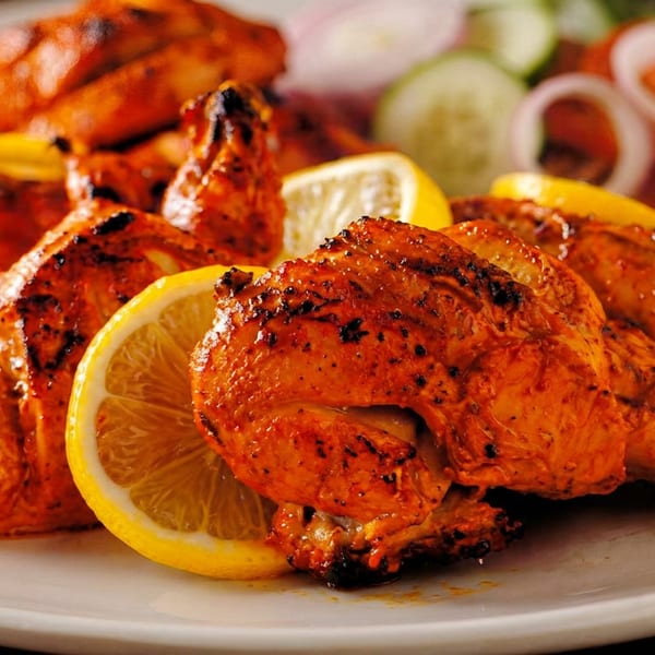 Grilled tandoori chicken pieces with lemon slices and a side salad on a white plate.