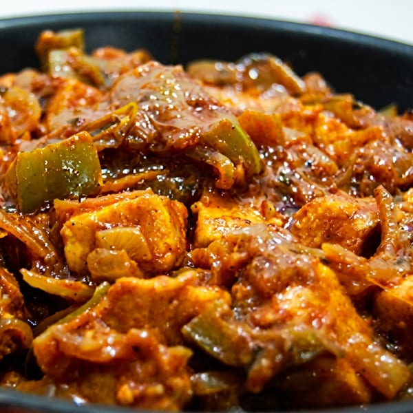 Close-up of paneer tikka masala with bell peppers and onions in a black pan.