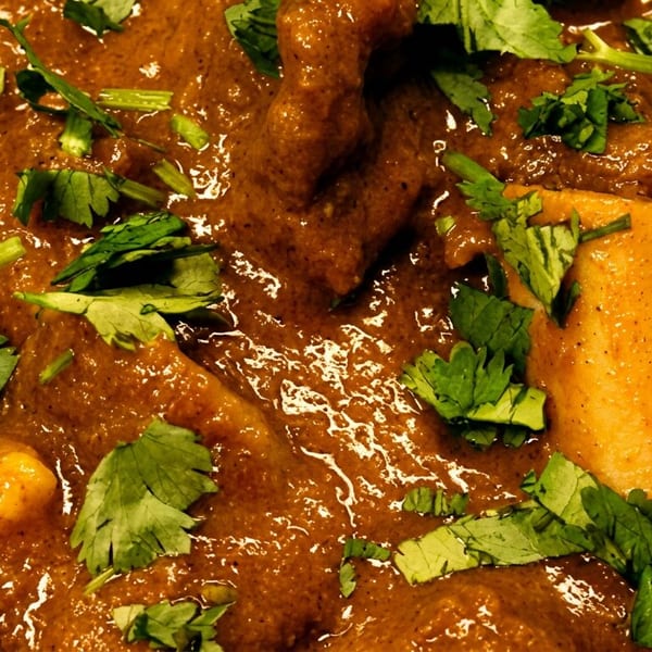 Rich brown curry with bone-in meat pieces and fresh green cilantro.